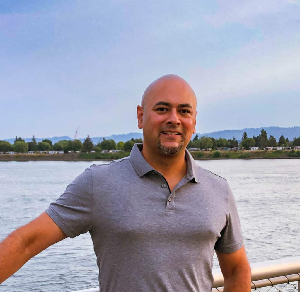 Man smiling by a river and trees.