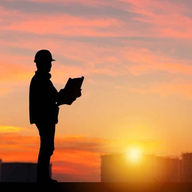 Silhouette of worker at sunset, holding plans.